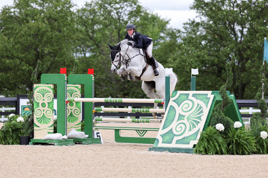 Karston Gundry jumping his horse over a green jump at a show